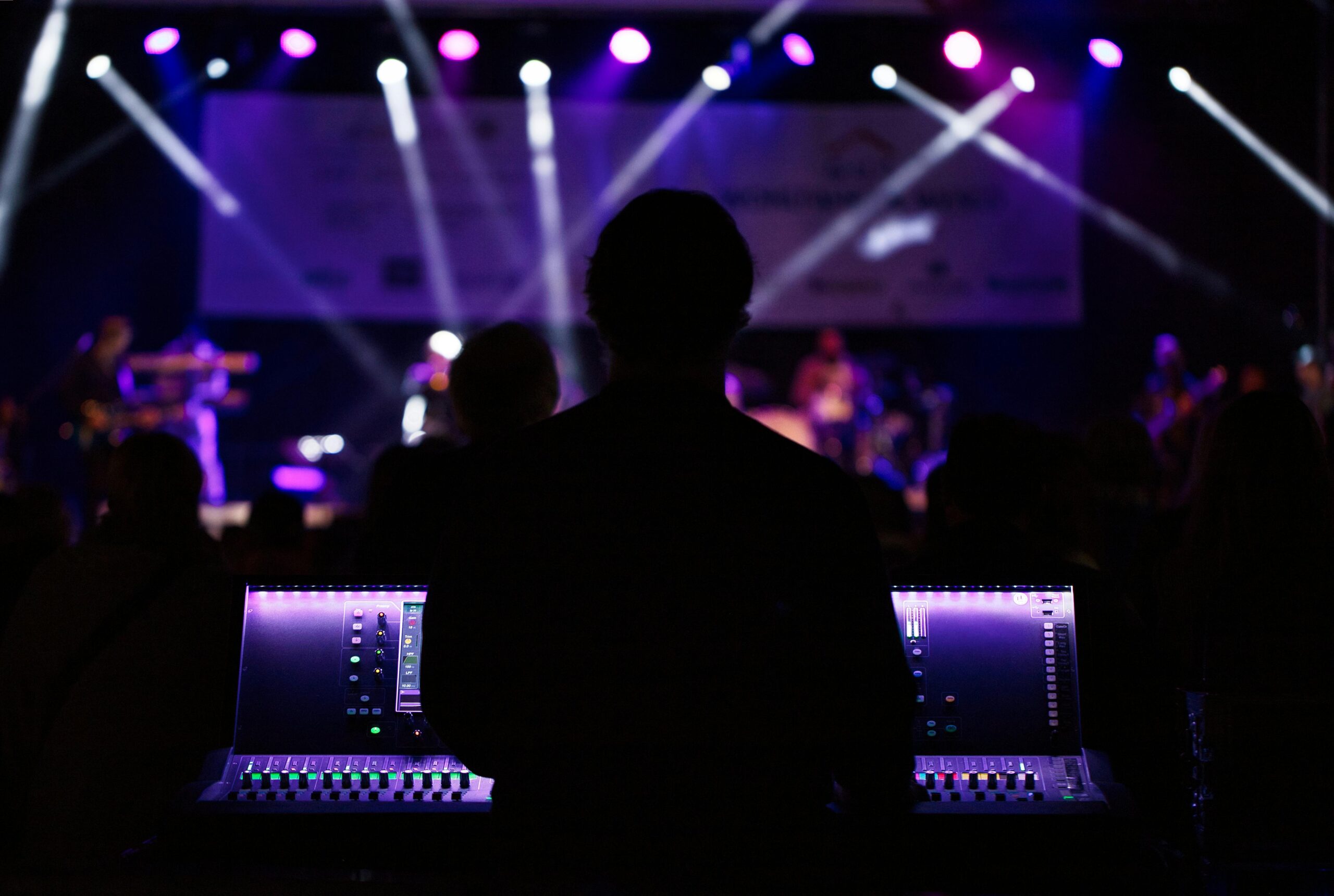A sound engineer manages the audio mixer during a vibrant live concert with colorful lighting.